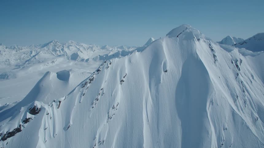 A skier stands atop a steep snowcovered mountain slope with visible rock outcrops