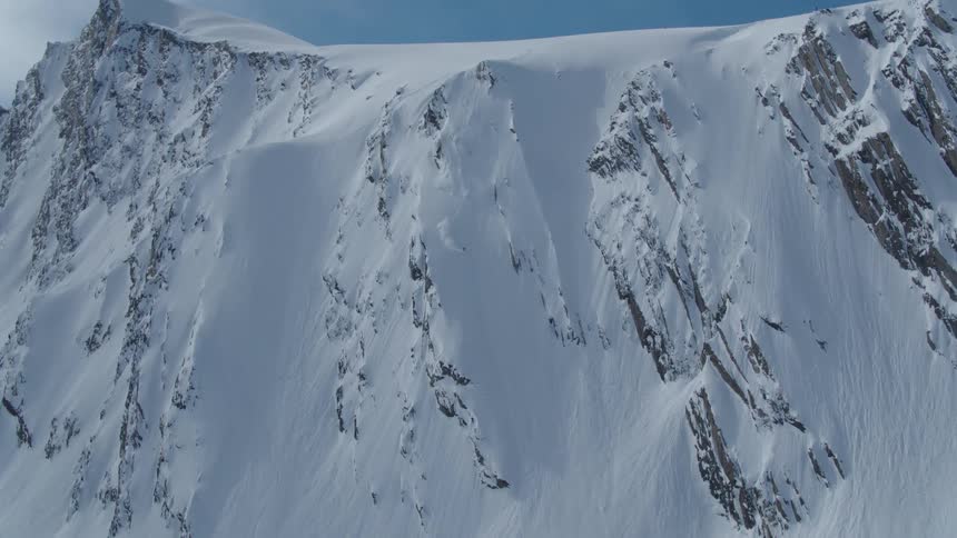 A skier descends a steep snowcovered mountain slope with visible rock outcrops