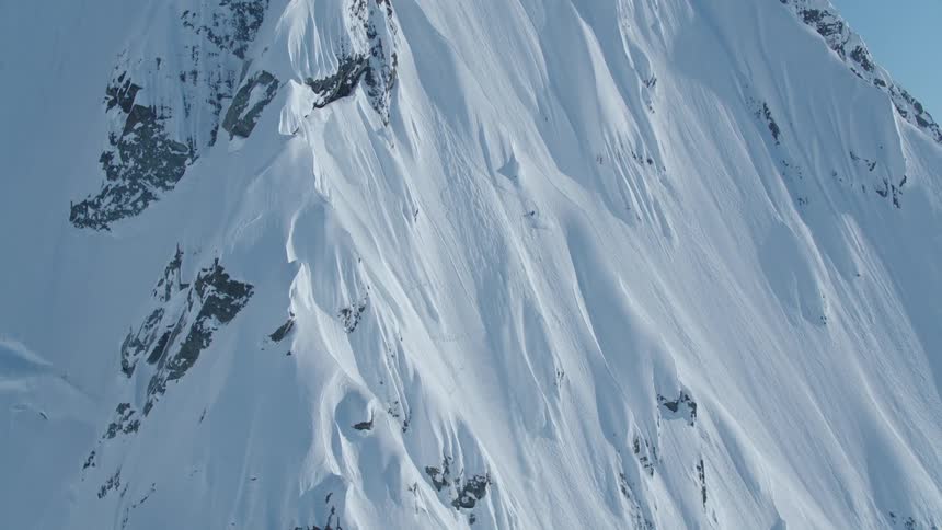 A skier descends a steep snowcovered mountain slope with visible rock outcrops