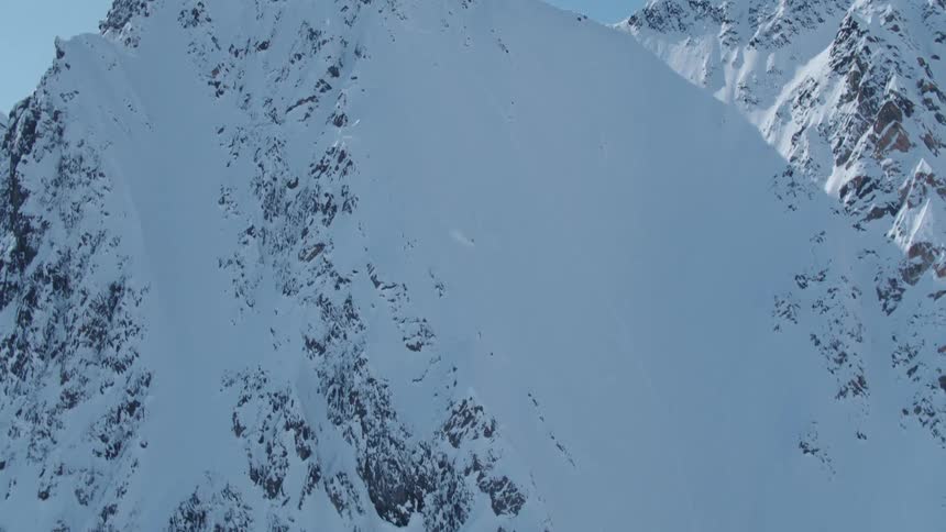 Aerial panorama of a person skiing down a large snowy mountain