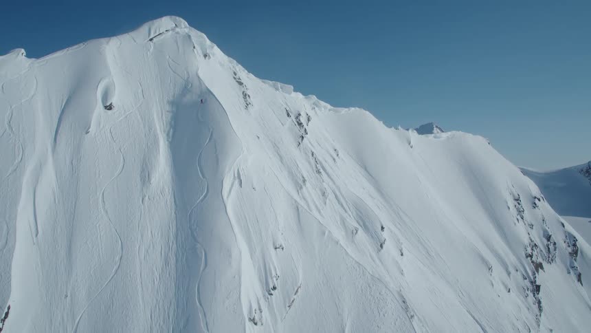 A skier descends a steep snowcovered mountain slope with visible rock outcrops