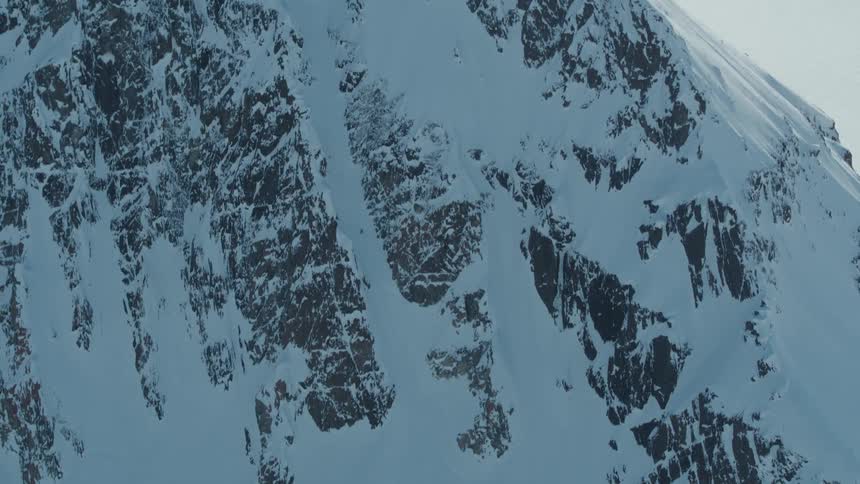 A skier descends a steep snowcovered mountain slope with visible rock outcrops