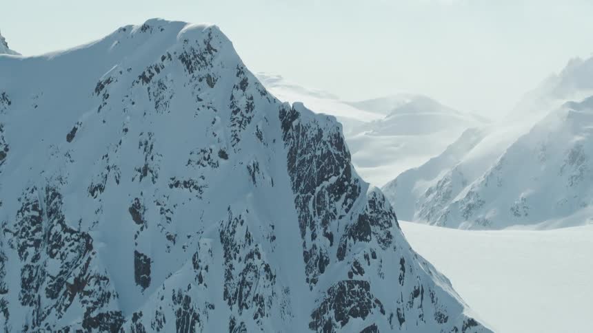 A skier descends a steep snowcovered mountain slope with visible rock outcrops