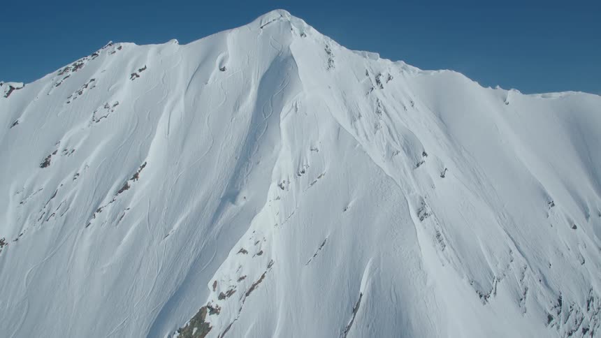 Aerial of a person snow skiing down a steep mountain on a sunny winter day