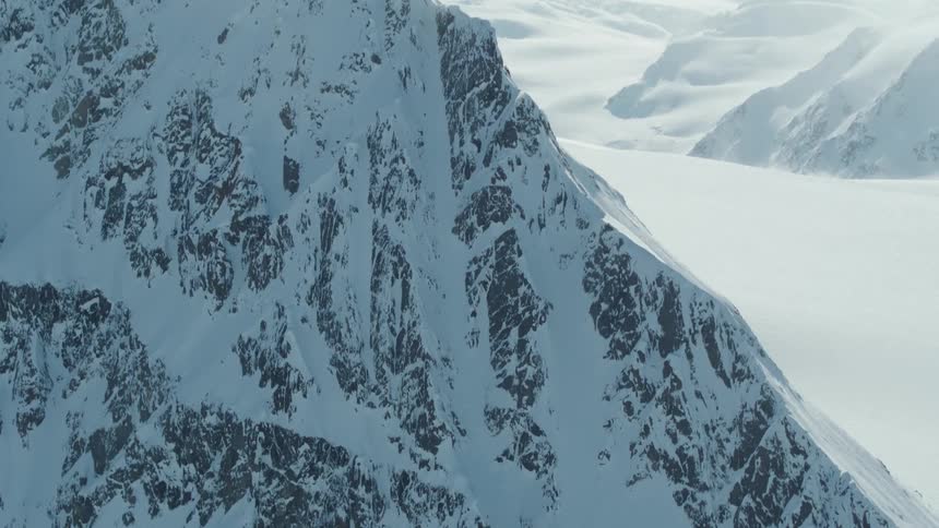 A skier descends a steep snowcovered mountain slope with visible rock outcrops