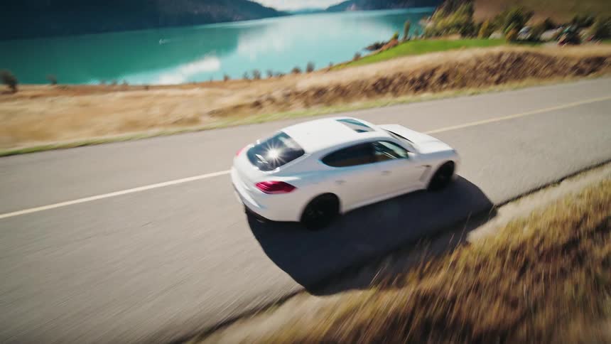Aerial shot of a white sports car traveling along a road in a natural environment