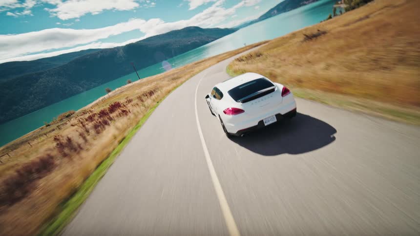 White car driving on a curving road with a large lake
