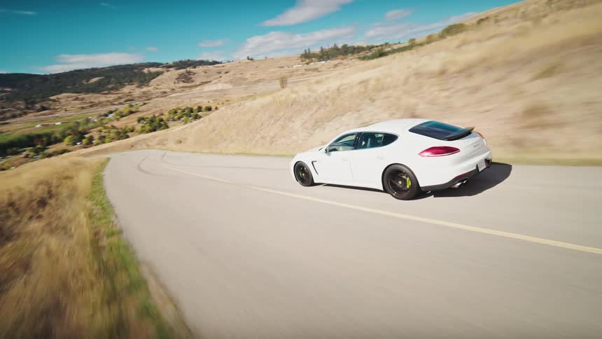 Aerial view of a white car traveling along a road in a natural environment during daytime