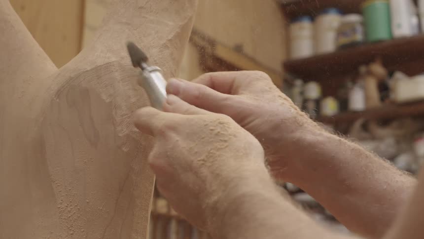 A man sands a piece of shaped wood in a shop