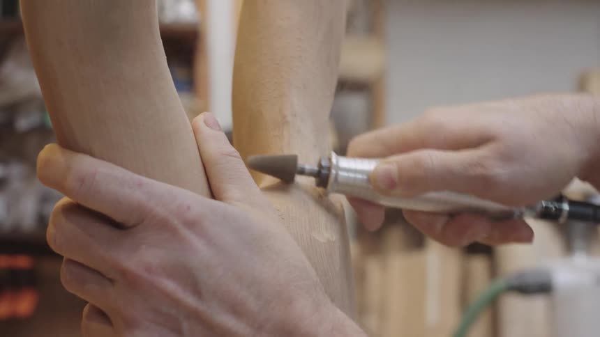 A person uses a rotary tool to shape a piece of wood