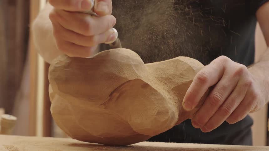 The woodcarvers steady hand guides the rotary tool carefully shaping the wooden sculpture into a work of art