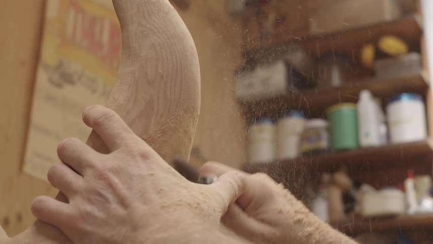 A sculptor uses a rotary tool to shape a piece of wood