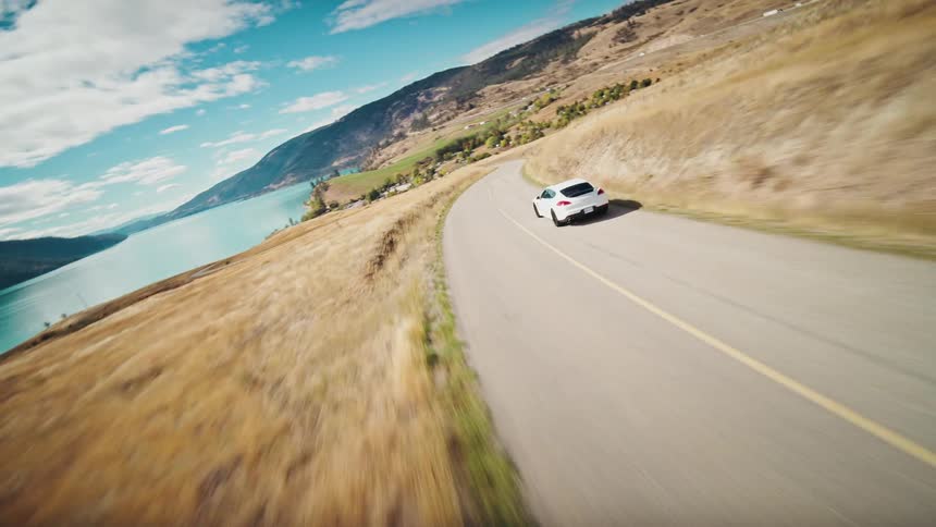 Aerial view of a white sports car traveling along a paved road by a lake