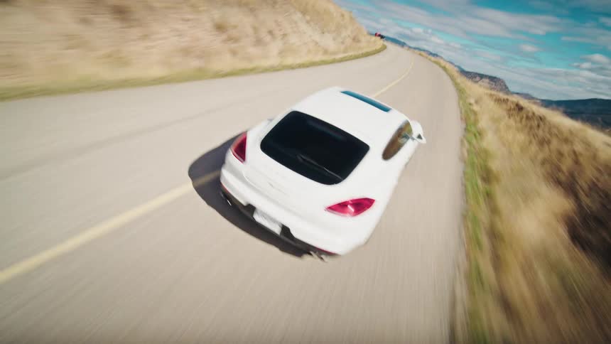 A sleek white porsche cruises along a winding road with a turquoise lake view