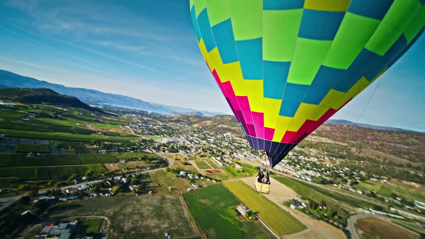 Aerial panorama of a large colorful balloon flying above an urban city and mountains
