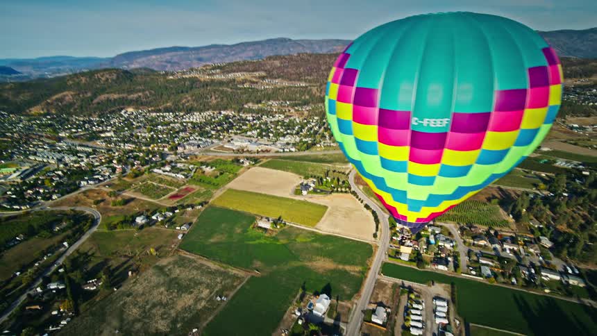 Aerial panorama of a colorful balloon flying above an urban city with mountains around