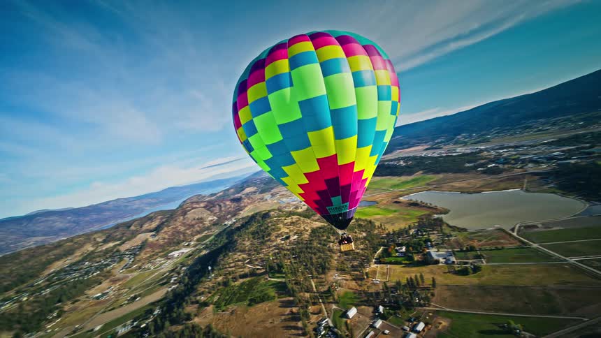 Colorful hot air balloon flying over a landscape that includes a city and farmland with hills in the background