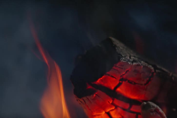 Wood of a campfire glows as it burns as smoke rises with the flames