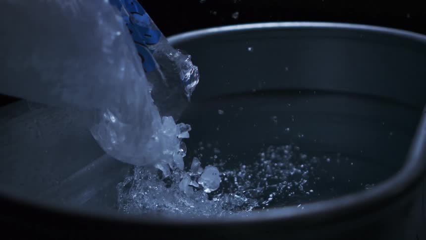Ice cubes are being poured into a metal bucket splashing water as they land
