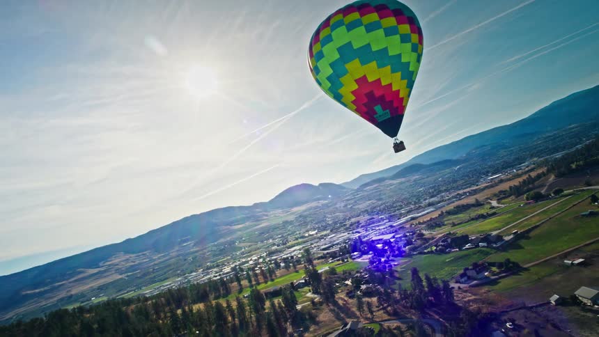 Aerial shot of a large colorful balloon flying above an urban city with mountains around