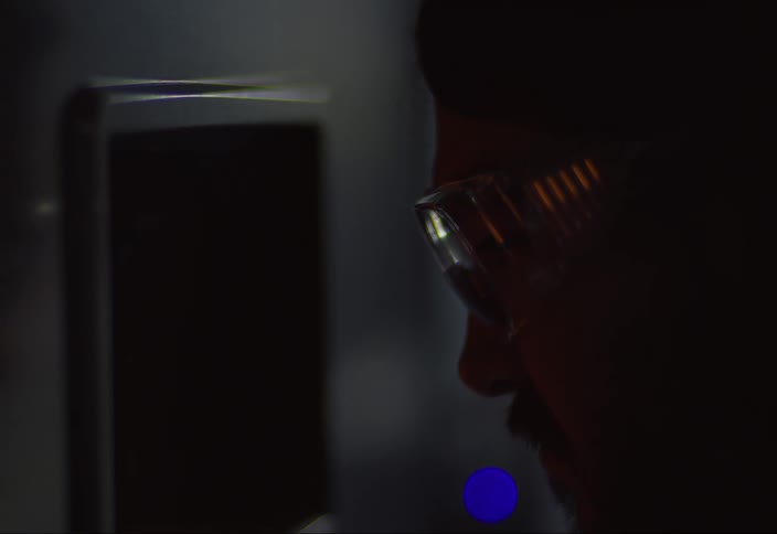 A man is looking at something in the dark wearing glasses