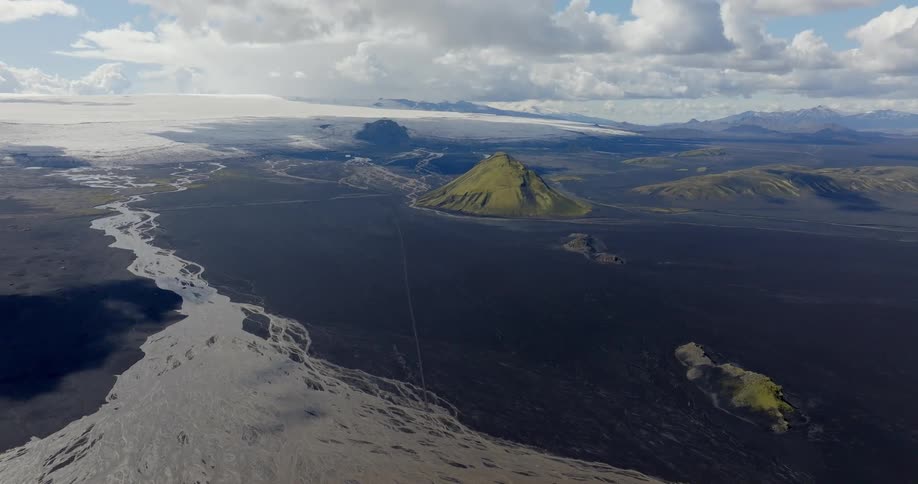 Aerial shot of a lake next to black soil and mountain valleys on the horizon