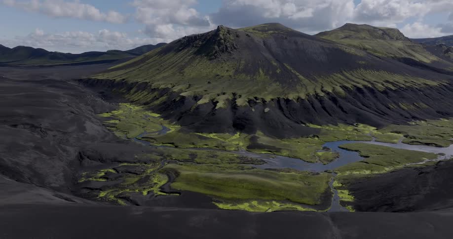 A white vehicle parked on a black dirt road through next to a rugged volcanic landscape