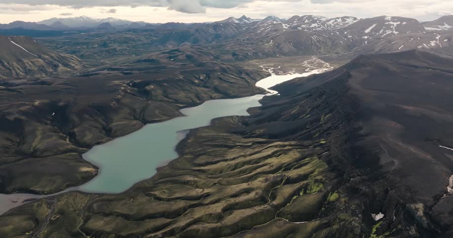 Aerial panorama of a mountain valley with a blue lake in the center and snowcapped mountains in the background
