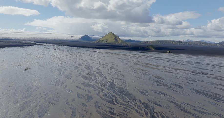 Rippled water surface with a prominent conical mountain in the background under a partly cloudy sky