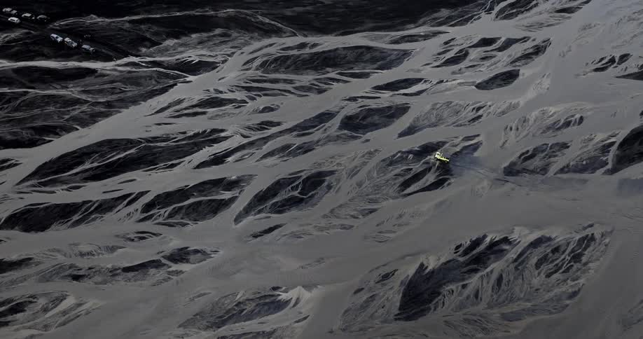 A small vehicle travels along a winding riverbed in a vast barren landscape