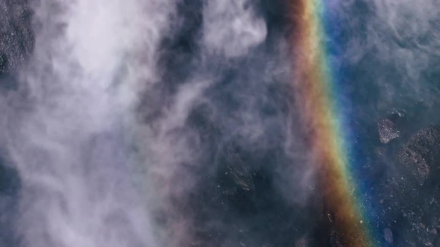 Aerial view of water gushing from a waterfall and a rainbow