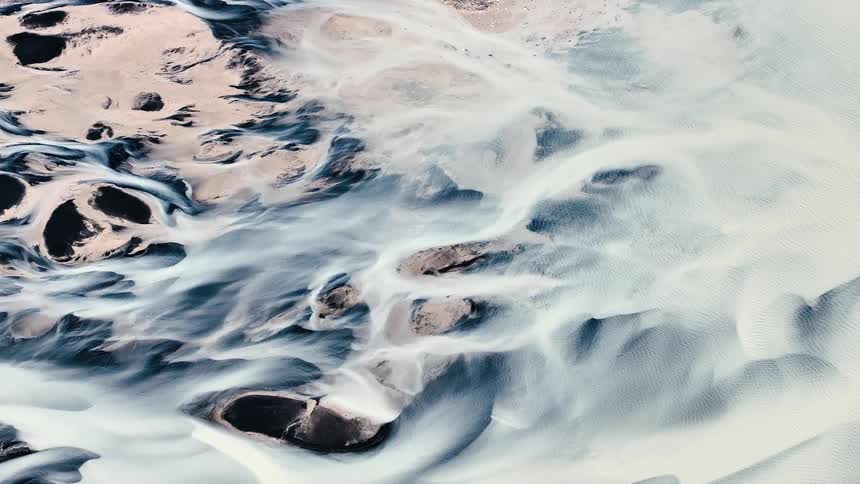 A winding glacial river flows through a barren desertlike landscape creating intricate patterns in the sand