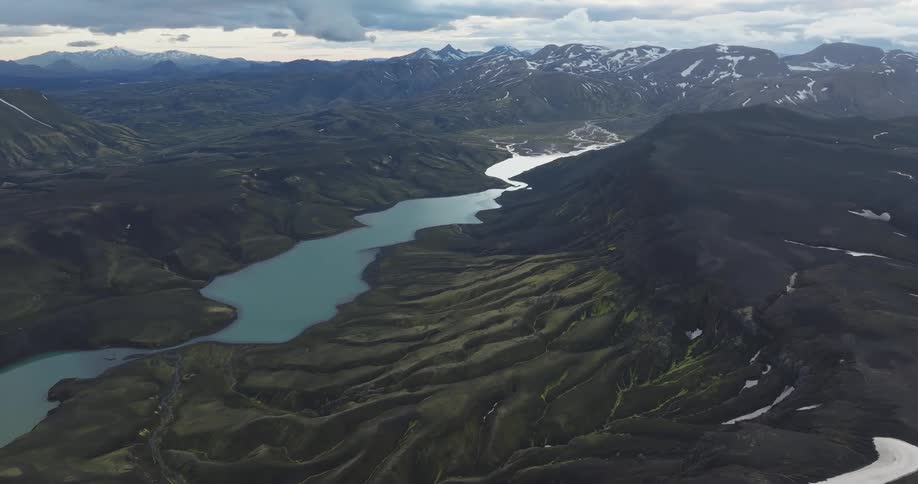 A winding river flows through a rugged volcanic landscape with a lake visible in the distance