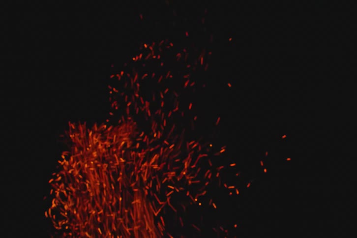 Campfire burning as sparks rise in the darkness