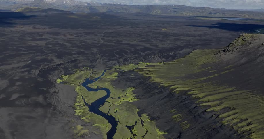 An aerial view of a winding river flowing through a rugged volcanic landscape