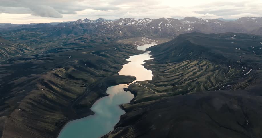 A winding river snakes its way through a rugged volcanic landscape reflecting the dramatic peaks and clouds in its still waters