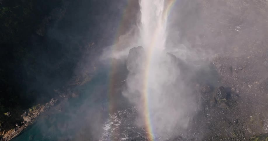 Closeup aerial of a rapidly cascading waterfall flowing over a rainbow