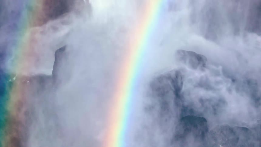 A rainbow arcs across a misty waterfall