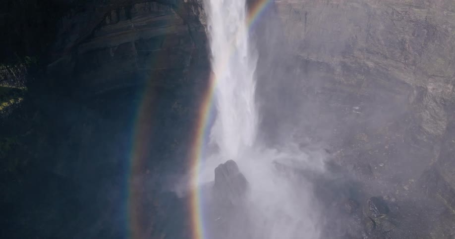 A rainbow surrounds a powerful waterfall cascading down a steep cliff