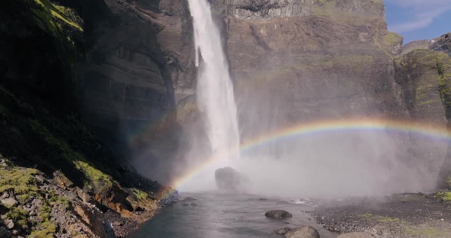 A powerful waterfall cascades down a rocky cliff with a rainbow arcing across the mist