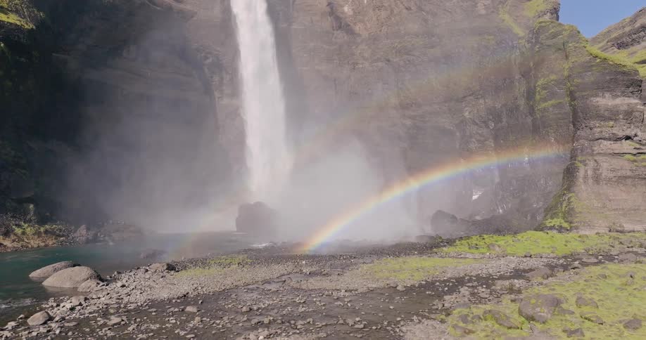 Waterfall cascading down a rocky cliff with a rainbow visible in the mist at the base