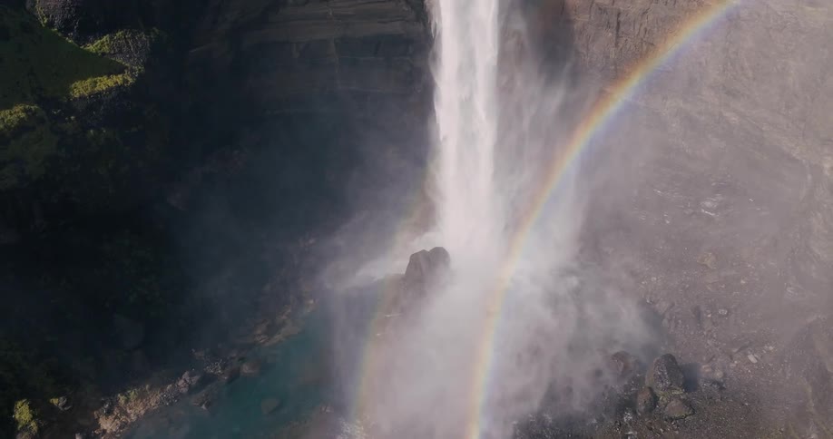 Large waterfall cascades down a rocky cliff forming a rainbow in the mist created by the water