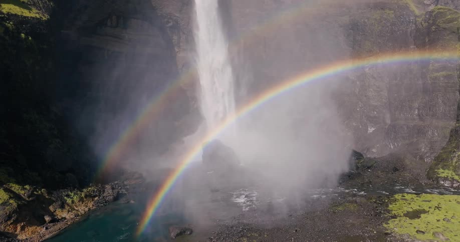 Waterfall cascading down a rocky cliff with a rainbow visible in the mist at the base