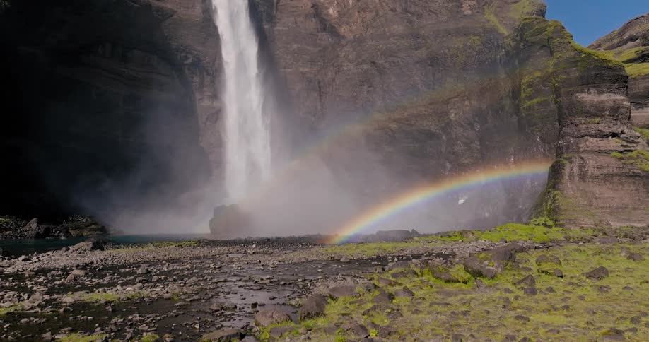 A rainbow arcs across the base of a powerful waterfall cascading down a rocky cliff