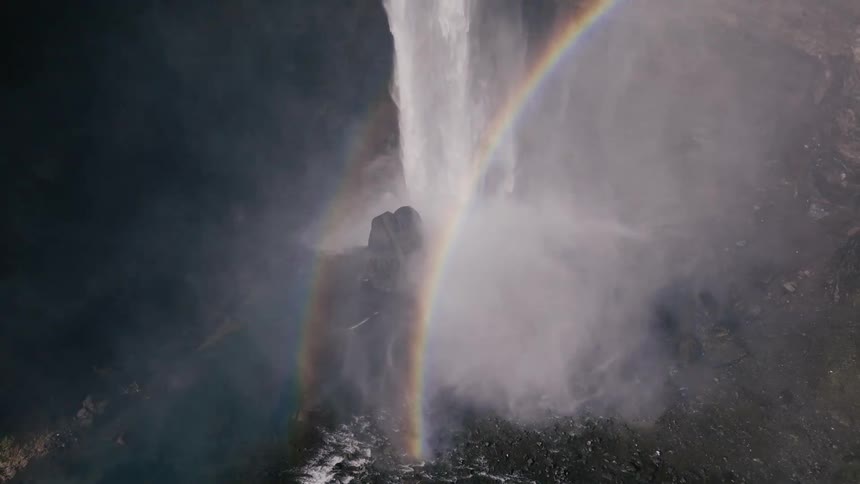 A rainbow surrounds a powerful waterfall cascading down a steep cliff