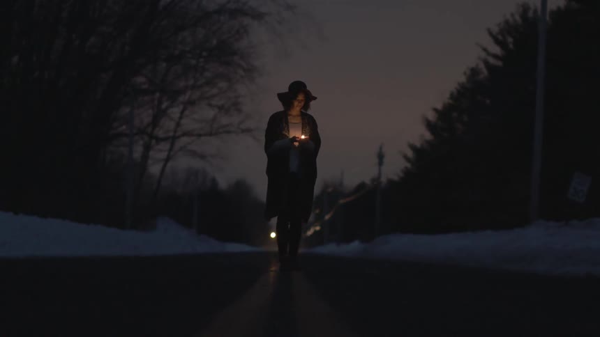 Woman holding a small light standing on a road at night
