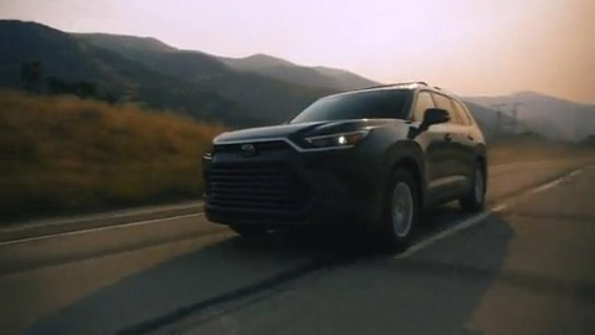 A black suv drives down a winding road at sunset