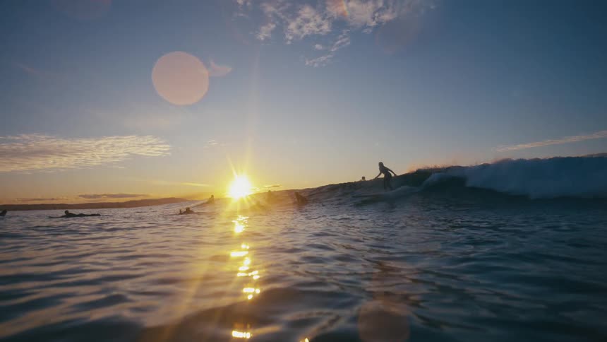Surfers riding small waves on a calm ocean at sunset