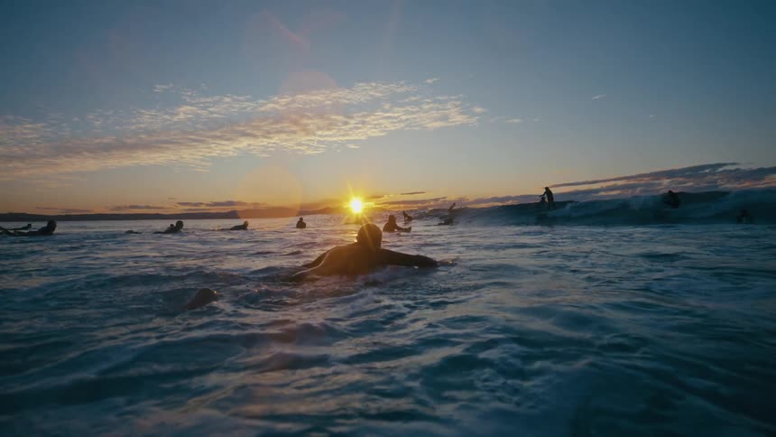 A group of people are surfing at sunrise