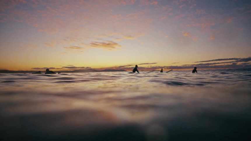 Group of surfers in the ocean during sunrise